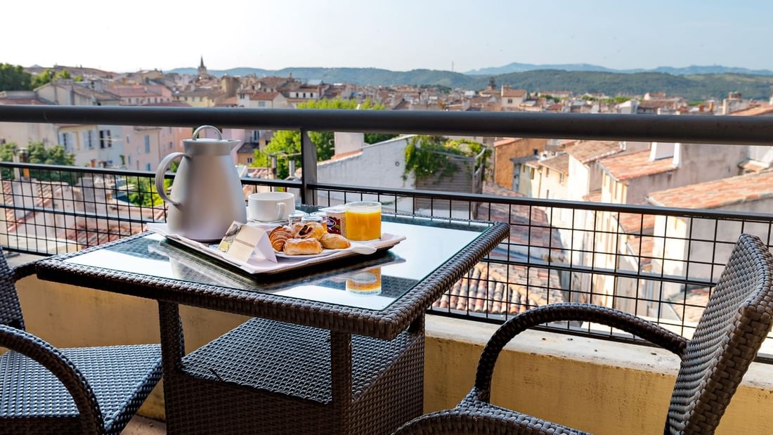 Terrasse avec vue sur la ville, table, deux chaises, et plateau avec nourriture et boissons.