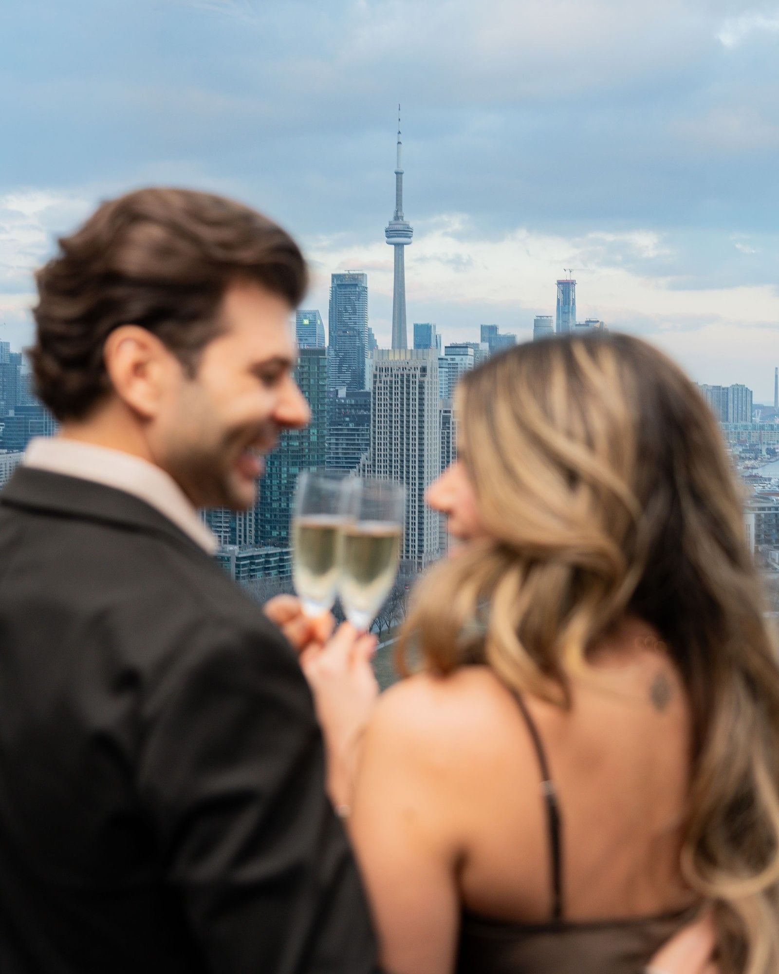Couple toasting champagne by the Toronto skyline with the CN Tower rising behind them during a stay at Hotel X Toronto