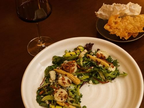 Plated salad with scallops and corn, next to a glass of red wine at La Cava de Santiago in Hacienda del Mar Los Cabos.