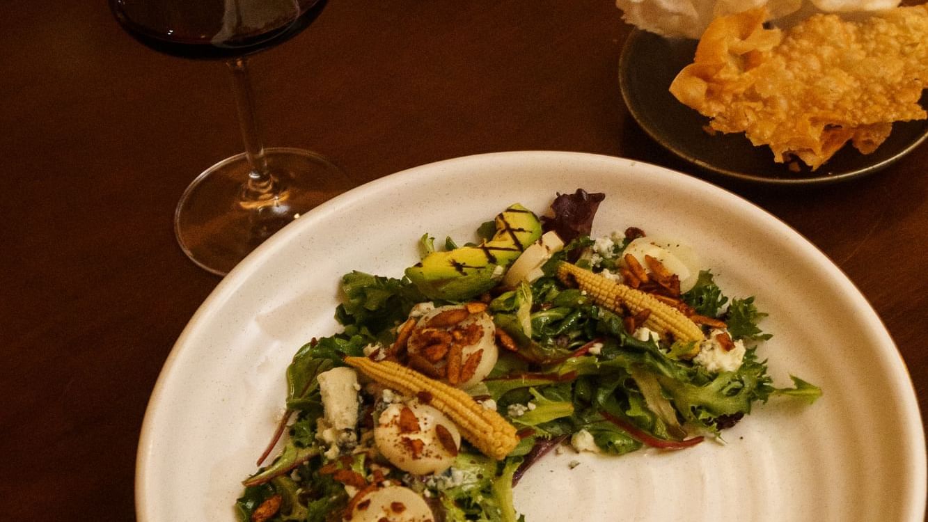 Plated salad with scallops and corn, next to a glass of red wine at La Cava de Santiago in Hacienda del Mar Los Cabos.