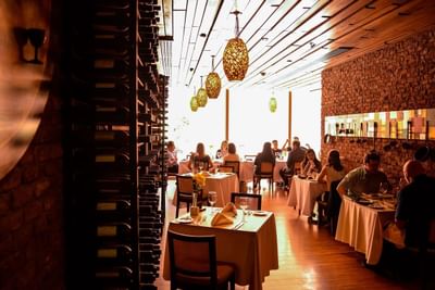 Huéspedes cenando en mesas blancas junto a muro de ladrillo bajo lámparas tejidas en Restaurante Fronterizo de NOI Vitacura