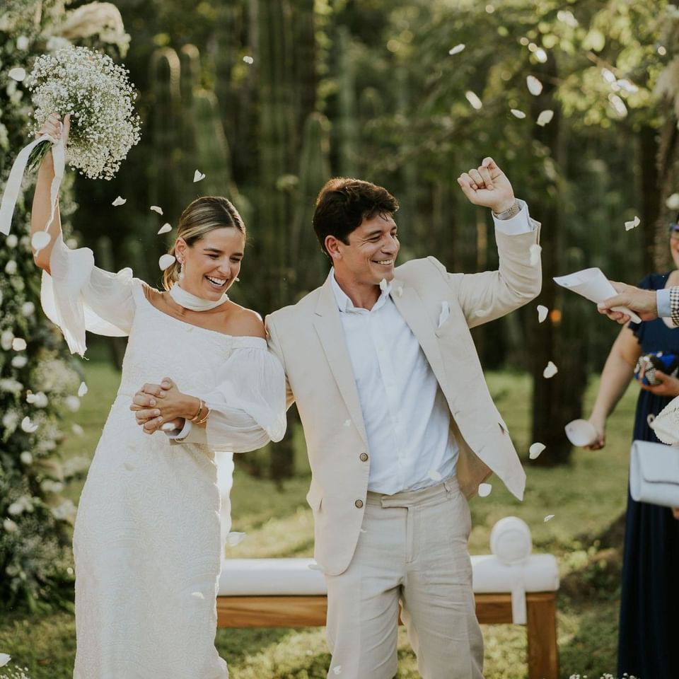 Pareja de recién casados celebrando con alegría mientras los invitados lanzan pétalos en una ceremonia al aire libre.