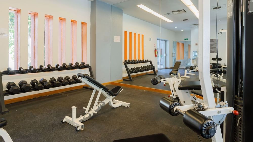 Well-equipped fitness center showing various dumbbells, a weight bench, and gym machines at Real Inn Torreon