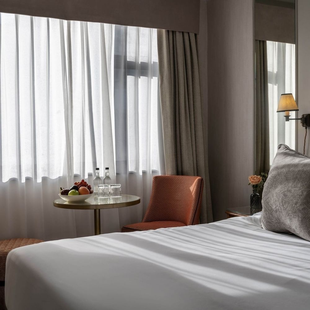 Cozy Standard Room with bed, pillows, fruit bowl, and window view at The Capital Hotel London.