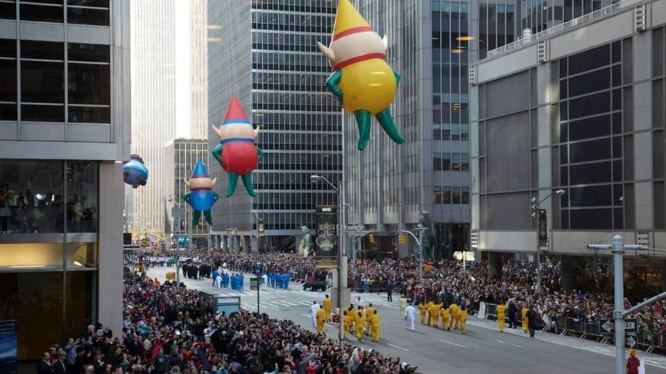 Large colorful elf balloons float above a crowded city street during a festive parade near Warwick New York