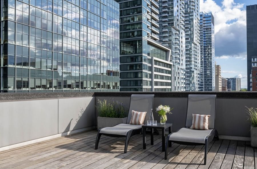 Two outdoor lounge chairs with pillows & a side table on a wooden deck in Penthouse Crescent at Warwick Le Crystal Montreal