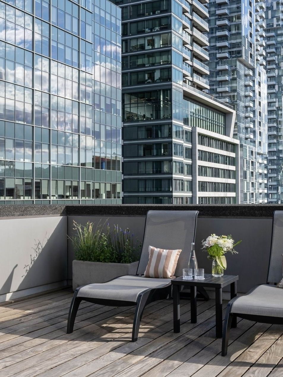Deux chaises longues avec des coussins et un arrangement floral sur une table, sur le balcon du penthouse du Warwick Le Crystal – Montréal.