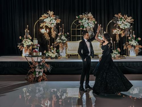 Couple dancing at wedding event with a decorative floral backdrop and candles in Sofitel Brisbane Central