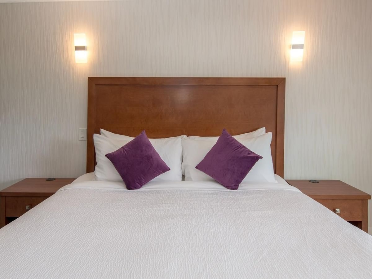 A bedroom with a white bed, two nightstands, purple pillows, and wall-mounted lights.
