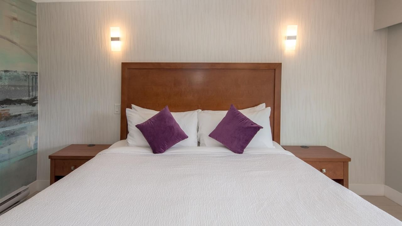 A bedroom with a white bed, two nightstands, purple pillows, and wall-mounted lights.