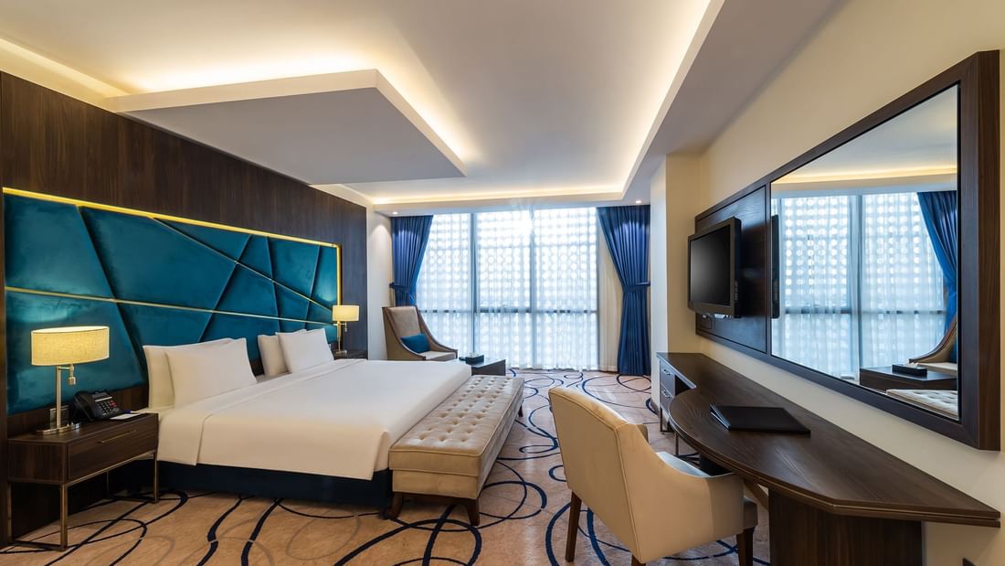 Comfy bed, TV with working table and lounge area in Deluxe Room at Warwick Riyadh
