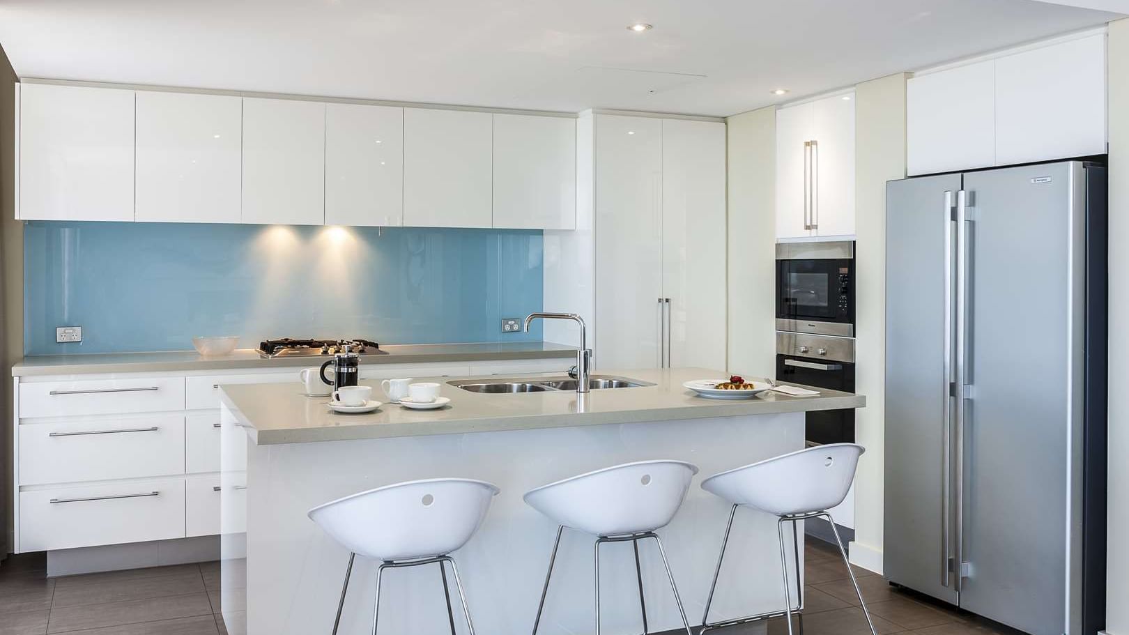 Modern kitchen in Interconnecting Apartment at The Sebel Mandurah with a large island and white bar stools