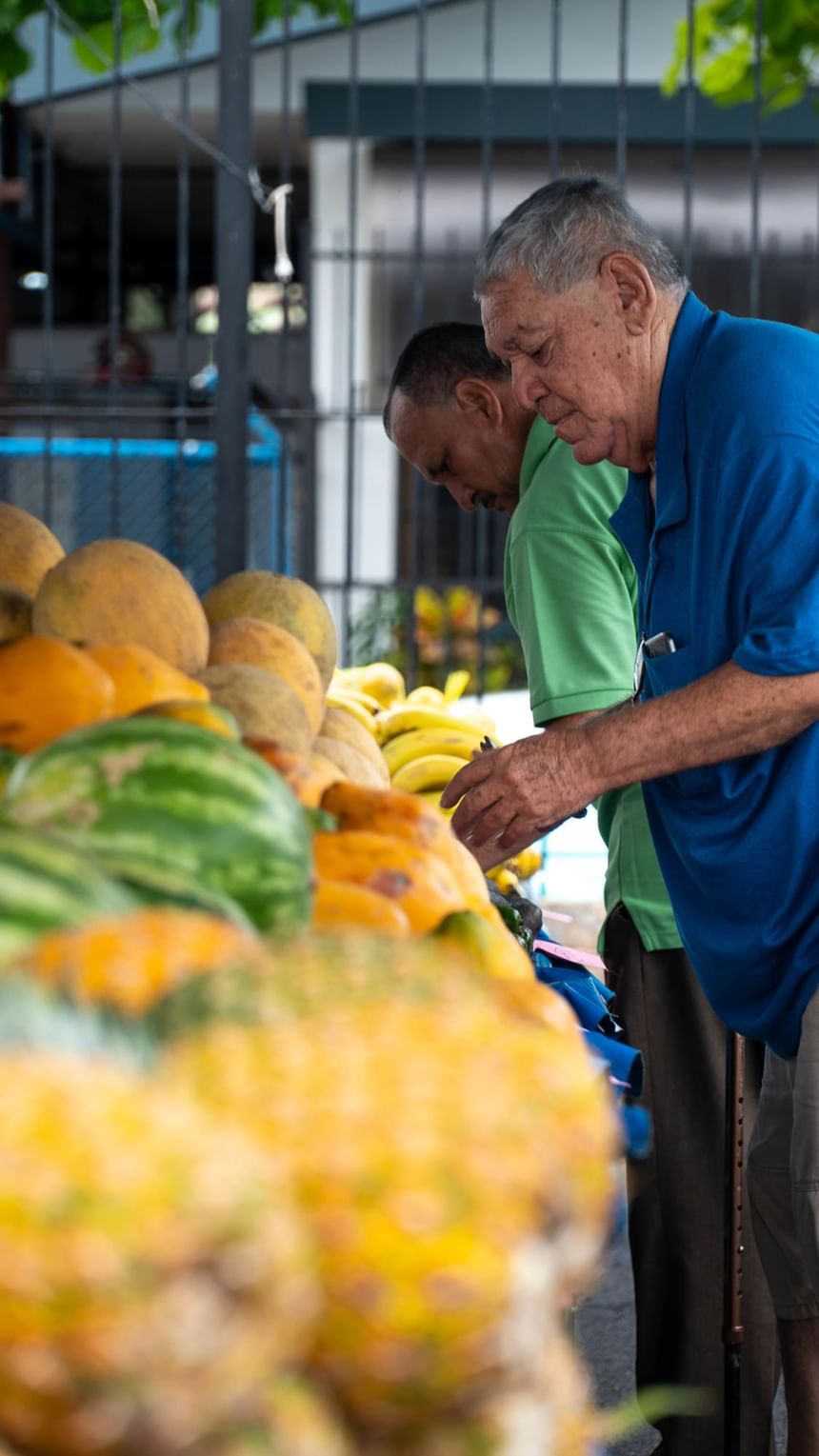 Two men selecting fresh fruit beside piles of pineapples and melons at the local market near Jungle Vista Boutique Hotel