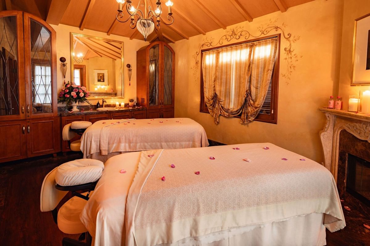 Elegant spa treatment room featuring two massage beds, a chandelier, and warm, classic wooden decor at Kelly's Spa