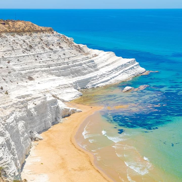 Weiße Felswand über einem Sandstrand und blauem Meer mit klarem Wasser.