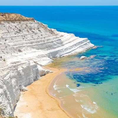 Weiße Felswand über einem Sandstrand und blauem Meer mit klarem Wasser.