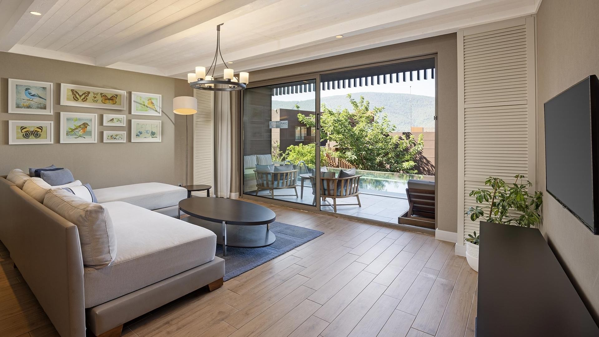 Современная гостиная зона семейного люкса Swim-up в Titanic Luxury Collection Bodrum с белым угловым диваном, деревянным журнальным столиком, ковром и плоским телевизором.