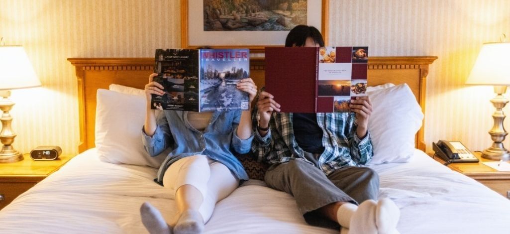 Guests relaxing on a hotel bed while reading travel guides in a comfortable Whistler guest room