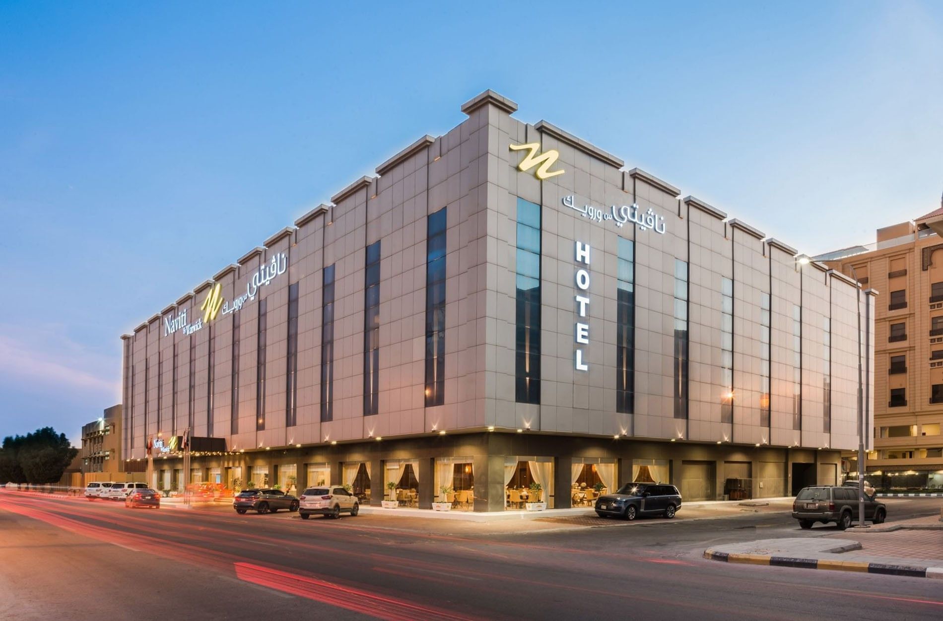Modern Naviti by Warwick Al Khobar building with illuminated signage and parked cars in front at dusk