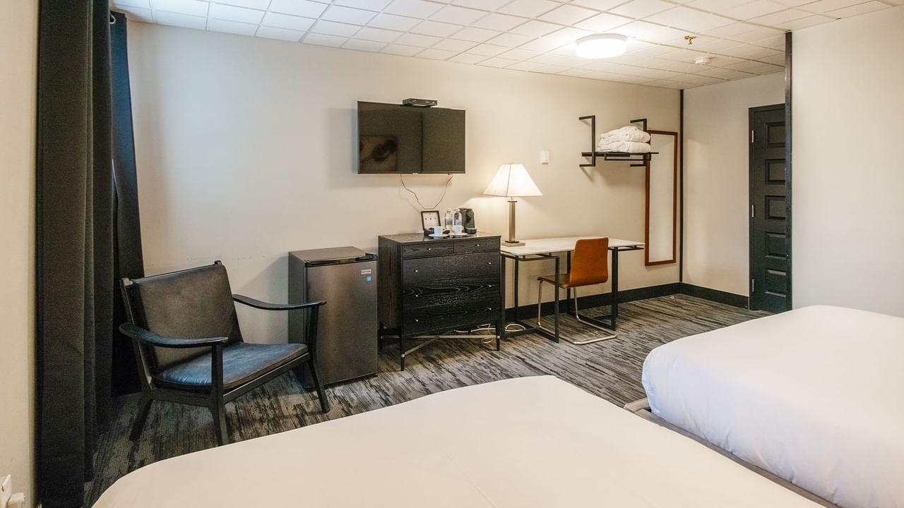 Hotel room with two queen beds, armchair, mini fridge, TV, and work desk