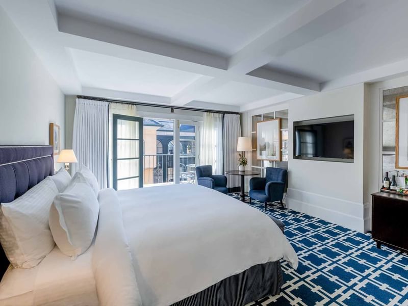 TV and seating area facing the cozy bed in Deluxe King Room with carpeted floors at El Prado Hotel