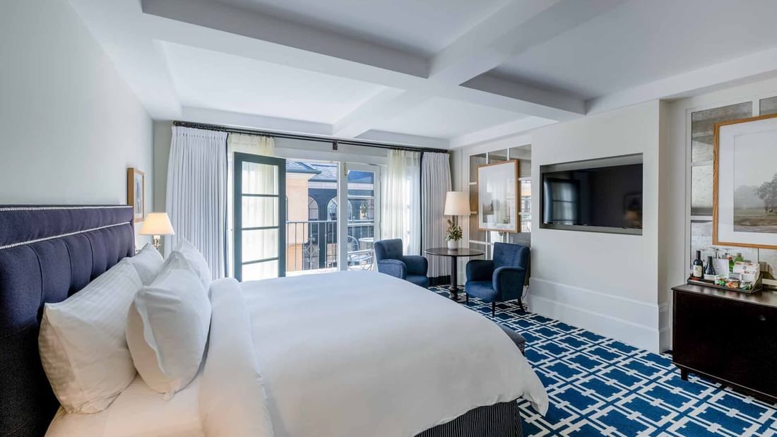 TV and seating area facing the cozy bed in Deluxe King Room with carpeted floors at El Prado Hotel