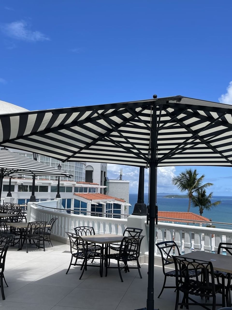 Café Bella Vista with striped umbrellas, black chairs, and tables, overlooking a serene ocean view at El Conquistador Resort