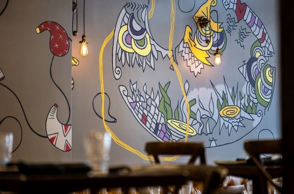 Colorful wall mural by hanging Edison bulbs near dark wooden chairs in BOTA at Warwick San Francisco