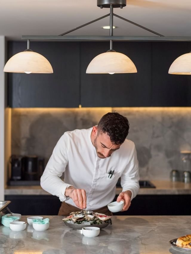 Chef at Elysium Manly plating fresh oysters on a marble counter under three dome pendant lights, a featured hotel in Manly
