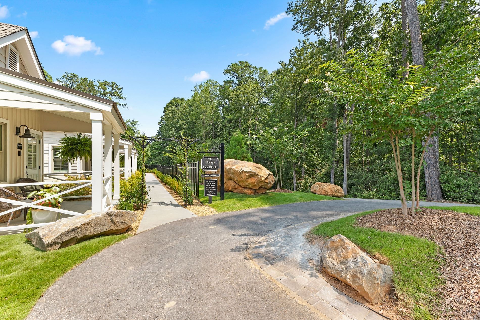 Scenic pathway leads to Cottages at Laurel Brooke through lush woods, with signs, large rocks, and a clear blue sky