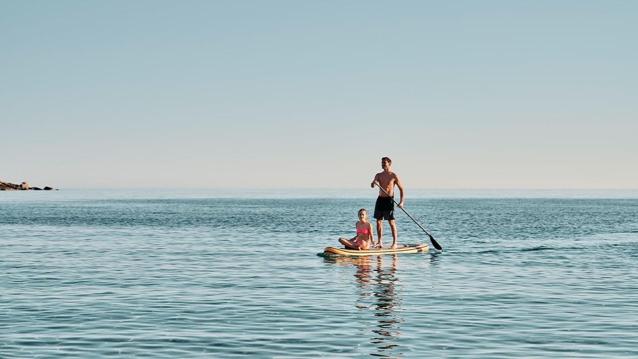 A man and a woman on a paddle board in the ocean on a clear day.