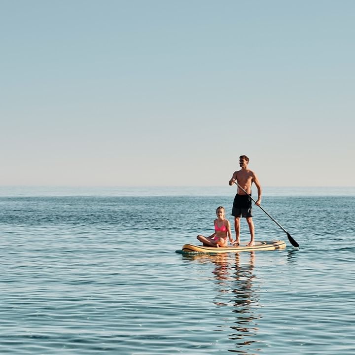 Uomo e bambina su un paddleboard, con l'uomo che pagaia nell'oceano.
