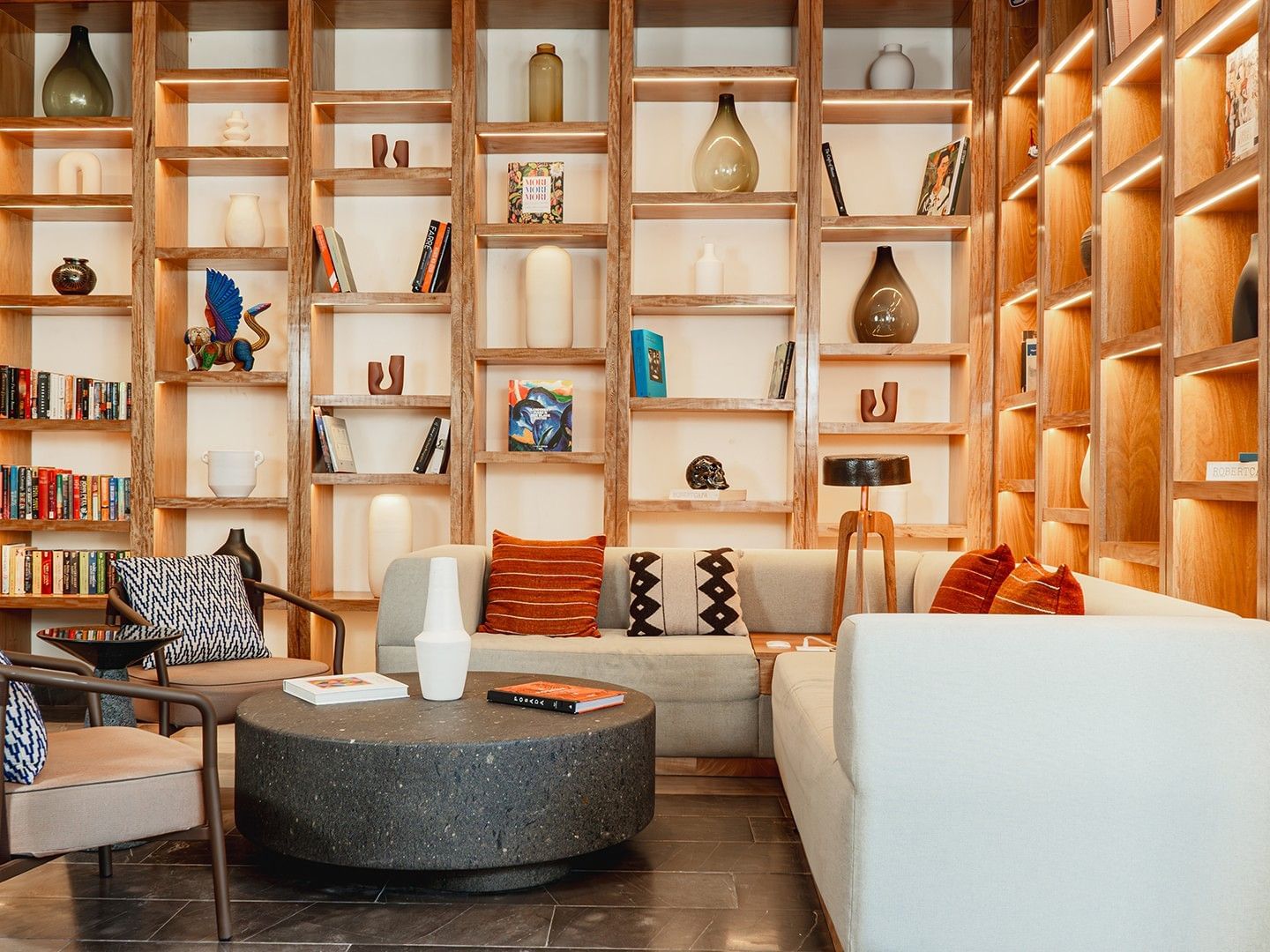 Cozy seating area with orange pillows and backlit shelves in Library Café & Deli at Camino Real Zaashila Huatulco