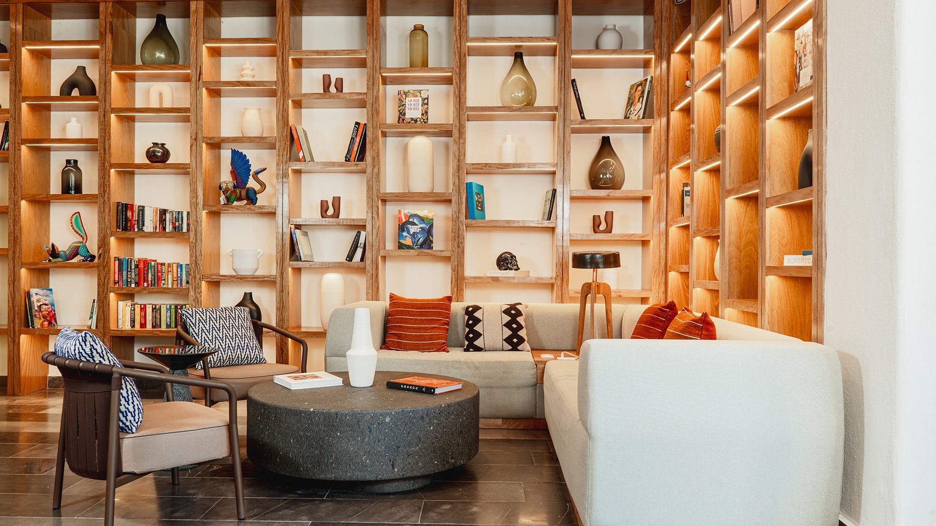 Cozy seating area with orange pillows and backlit shelves in Library Café & Deli at Camino Real Zaashila Huatulco