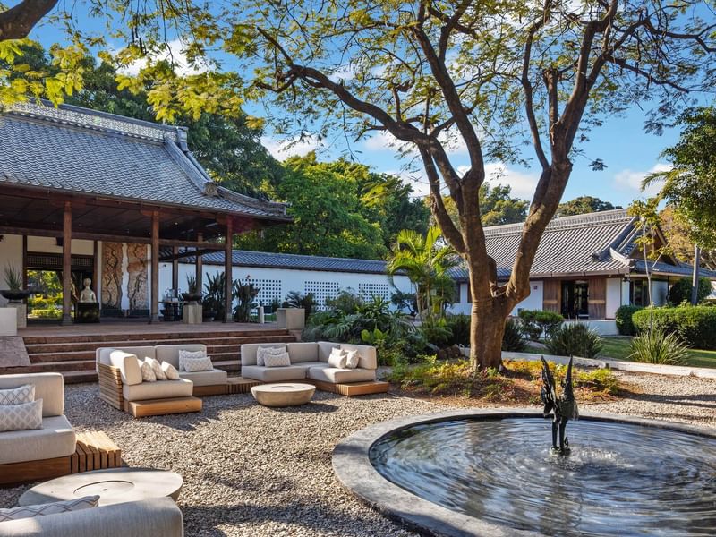 Outdoor seating area with sofa, tables, and fountain in a serene garden at Grand Fiesta Americana Sumiya Cuernavaca.