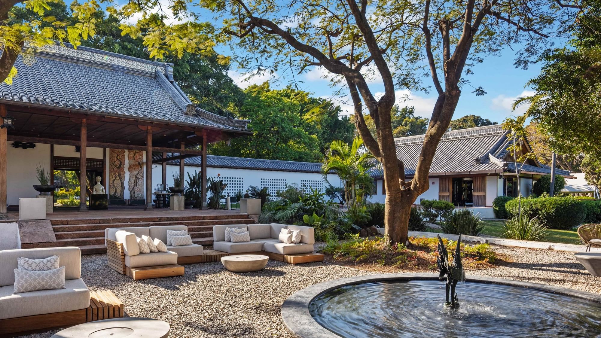 Outdoor seating area with sofa, tables, and fountain in a serene garden at Grand Fiesta Americana Sumiya Cuernavaca.