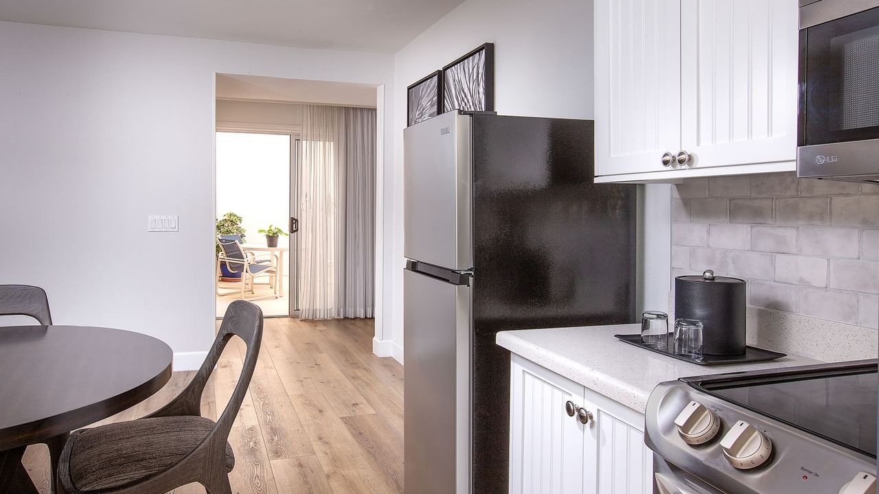 A modern kitchen with a black refrigerator, white cabinets, a dining area, and a sliding glass door.