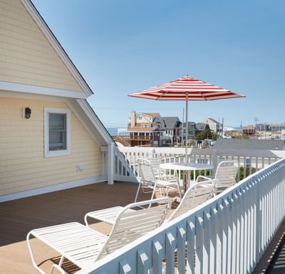 Bright deck with white lounge chairs and a red-and-white striped umbrella, overlooking beach houses at The Hotel Maria