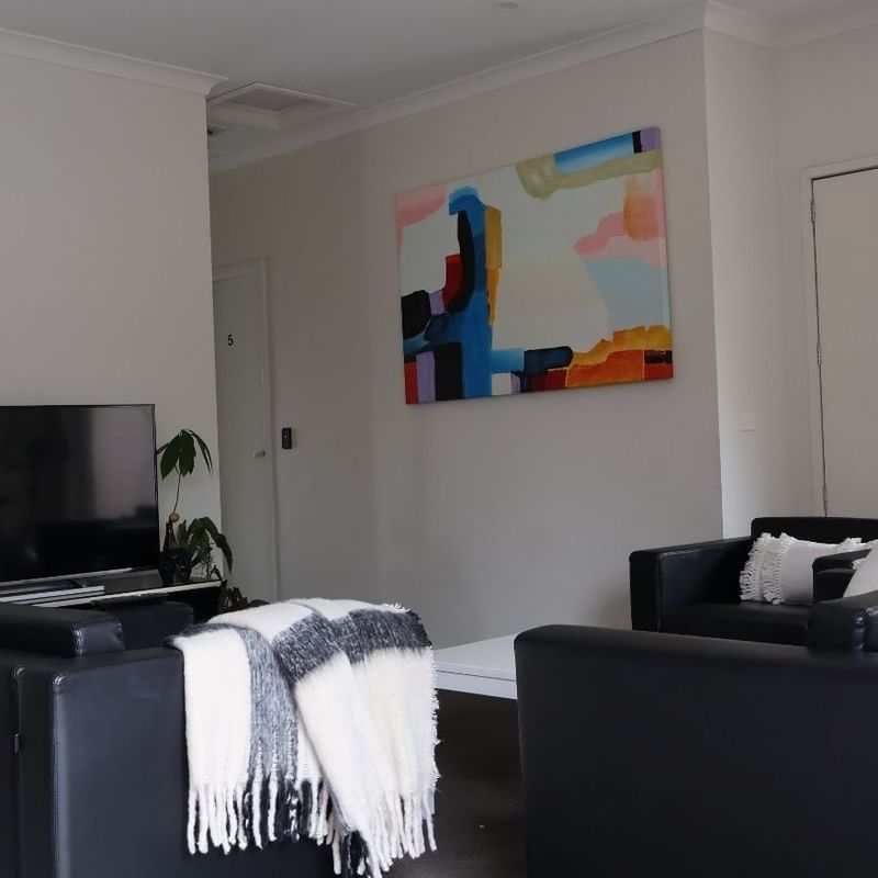 Black couches, TV, and colorful abstract painting in a modern living room at La Trobe University Regional Housing.