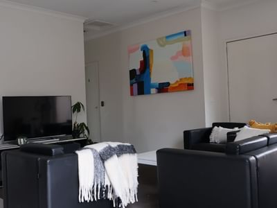 Black couches, TV, and colorful abstract painting in a modern living room at La Trobe University Regional Housing.