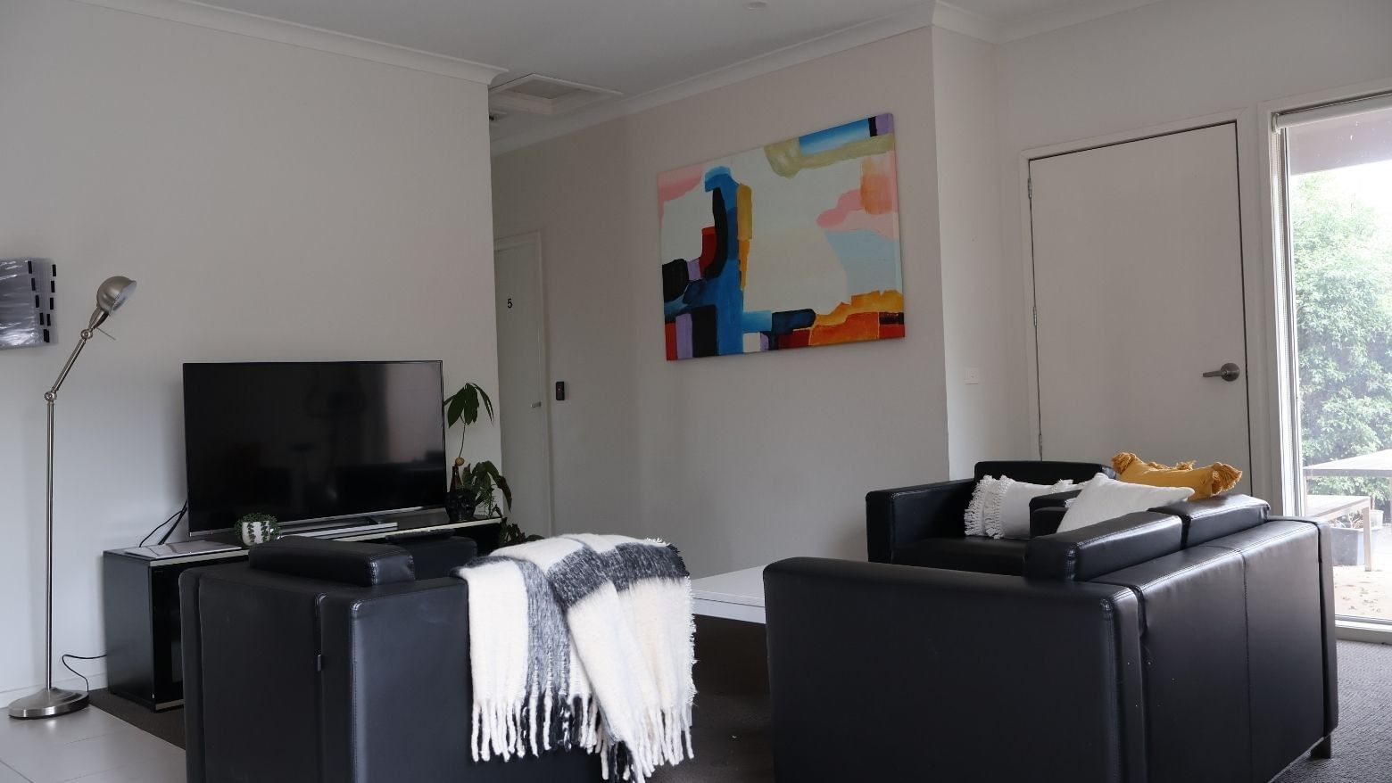 Black couches, TV, and colorful abstract painting in a modern living room at La Trobe University Regional Housing.