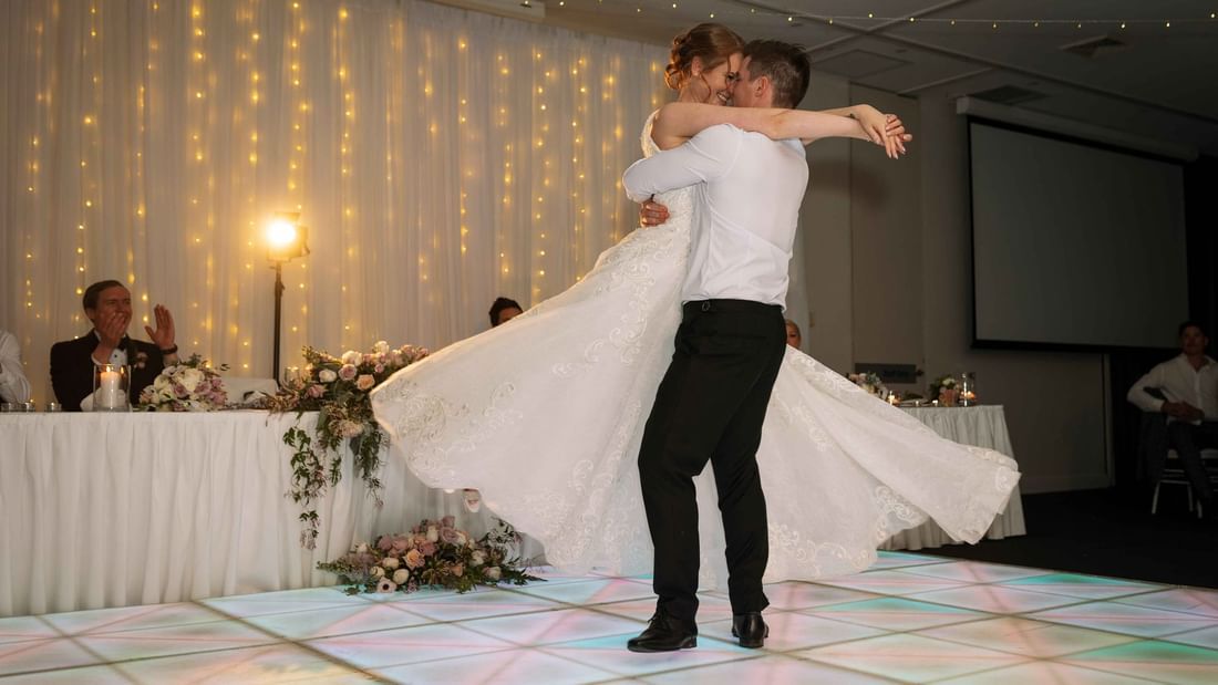 A couple dancing in a room with fairy lights and a floral arrangement at Mercure Kooindah Waters