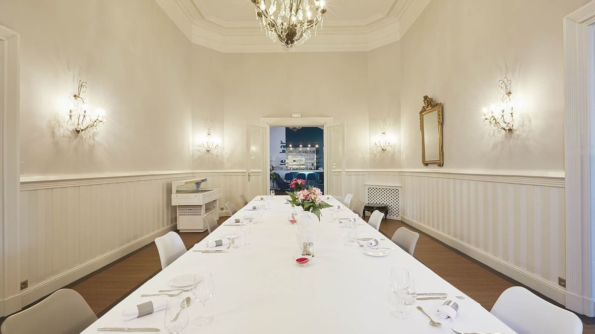 Salle de réception élégante avec une longue table, des chaises blanches, un lustre et des lustres muraux.