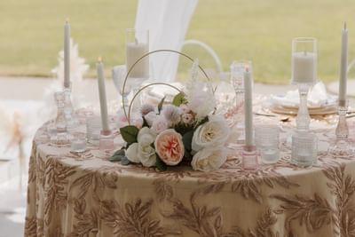 Floral centerpiece with pink & white roses alongside tall candles on a table in Spencer Meadows Pavilion at Spencer Hotel