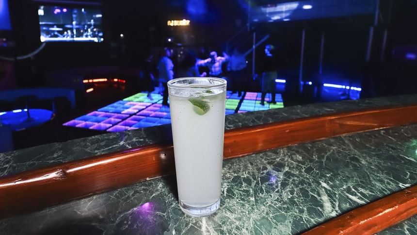 Cóctel con hielo y lima en barra de mármol, con pista de baile iluminada y gente en El Rollo de Araiza Palmira 