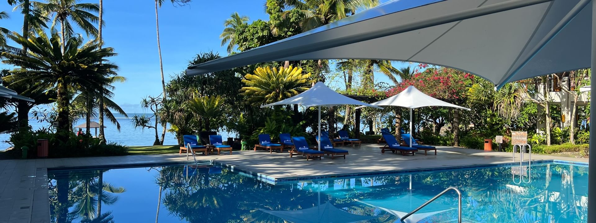 Blue lounge chairs by a pool under white umbrellas surrounding tropical palms at Warwick Fiji Resort and Spa in Korolevu