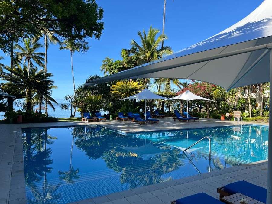 Blue lounge chairs by a pool under white umbrellas surrounding tropical palms at Warwick Fiji Resort and Spa in Korolevu