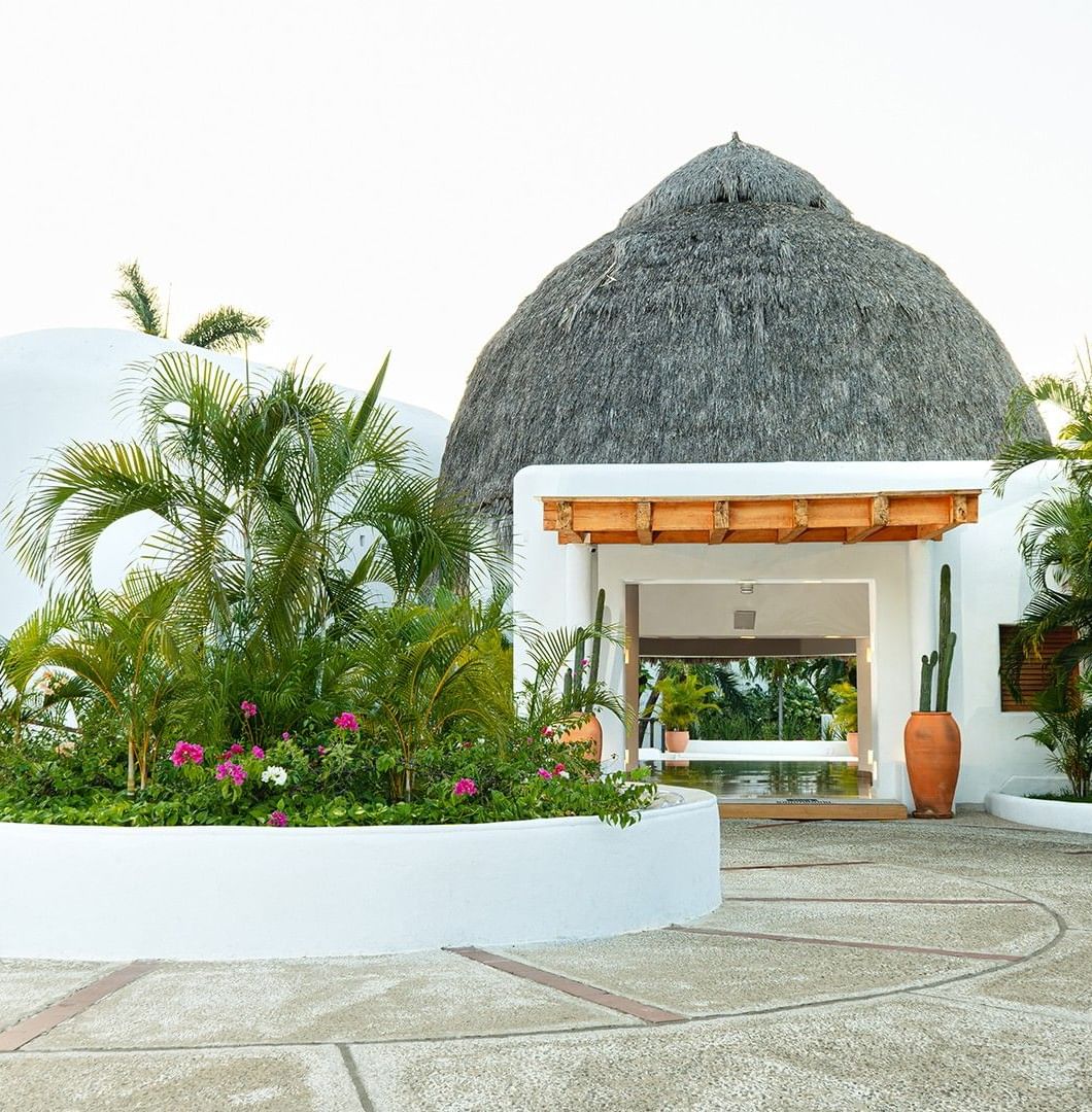 Exterior view of Camino Real Zaashila Huatulco entrance with lush greenery and thatched-roof huts