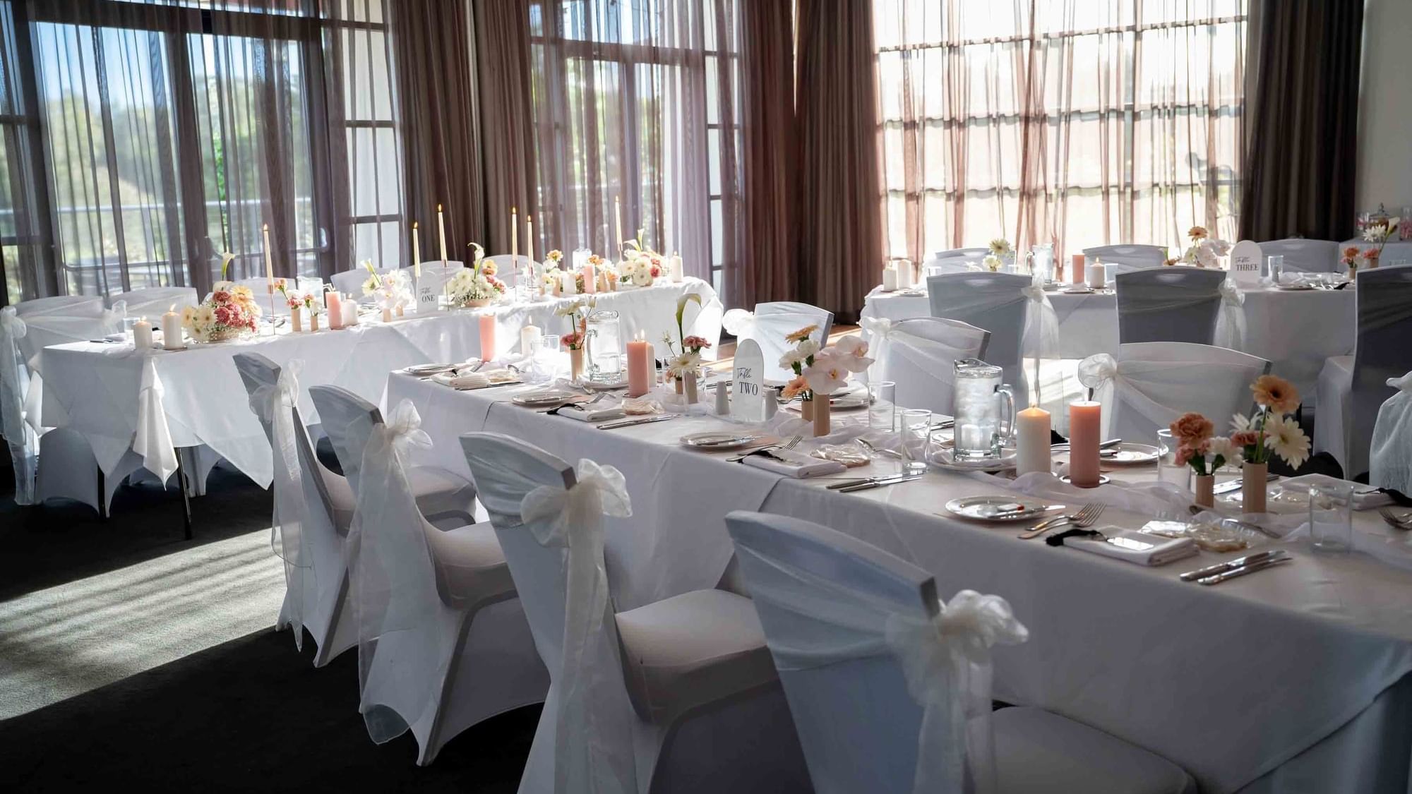 Wedding reception setup with white tablecloths, floral centerpieces, and candles at Mercure Kooindah Waters