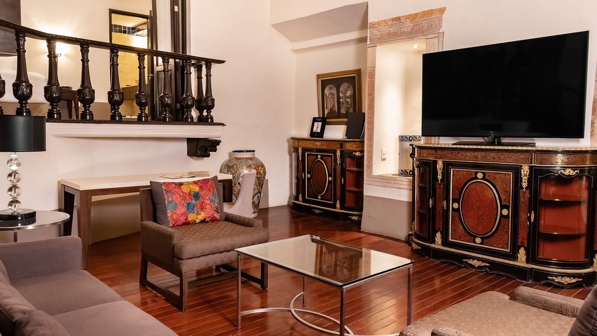 Living area with antique cabinets, a glass coffee table, and a brown chair in King Presidential Suite at Quinta Real Puebla